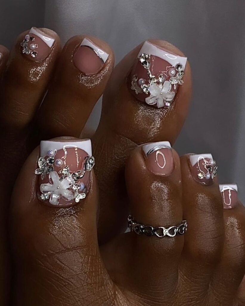 Las uñas de los pies de una mujer están decoradas con flores y anillos.