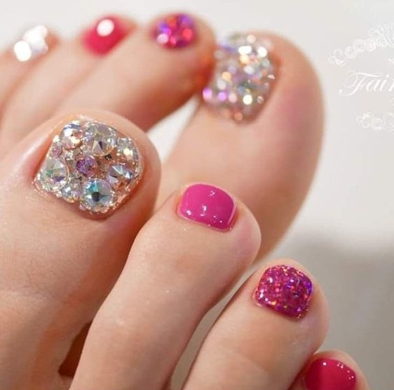 Los dedos de los pies de una mujer están decorados con pedrería y esmalte de uñas rosa.