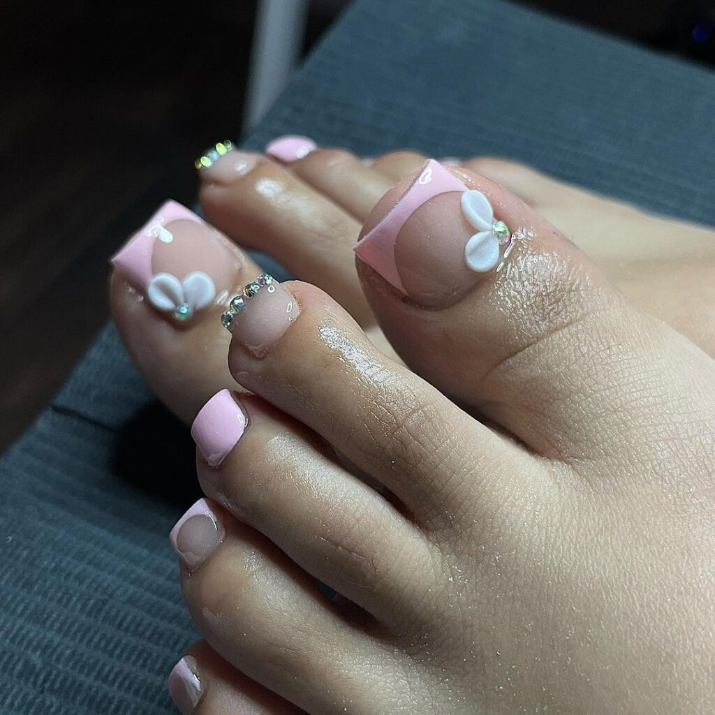 Los pies de una mujer con uñas rosadas y blancas.
